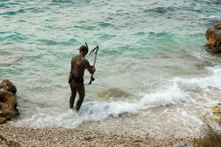 Underwater fishing. A man in a wetsuit with a water gun in his hands plunges into the water.の写真素材