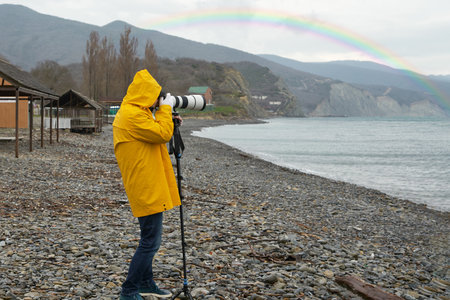 A man photographs a rainbow on the beach with a long-focus lens resting on a monopodの写真素材