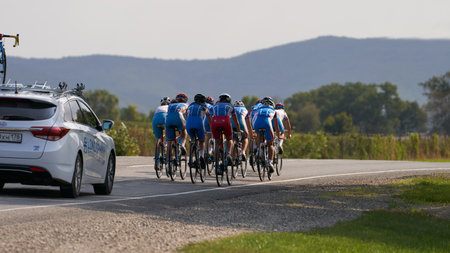 Russia, Anapa, September 16, 2021: training run of the women's cycling team. A group of cyclists riding on the highway in the mountainous terrain. They are followed by a coach in a car.のeditorial素材