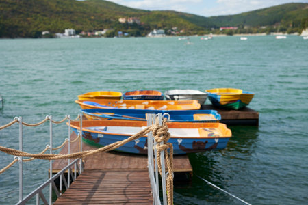 A pier with colored boats on a lake surrounded by green mountains.