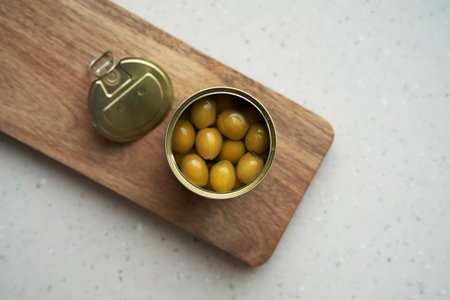 Seedless canned green olives in a tin opened with a key, embedded in the lid. The lid is next to it. top view.の写真素材