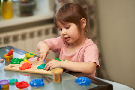 The little girl is carving plastic figures out of the house at the table.の写真素材