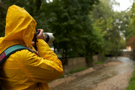 Landscape photography in the rain. Photographer in a raincoat taking photos in a park.の写真素材