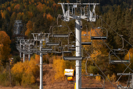 A chairlift with many chairs in the air against the picturesque yellow backdrop of the fall mountains.の写真素材
