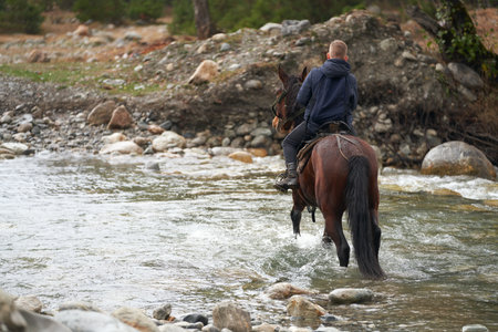 A child on horseback crossing a stony bed of a mountain river with a fast current. Copy space.