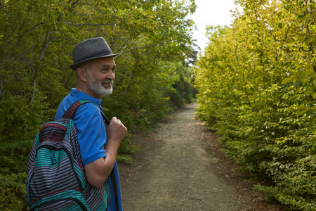 An adult male hiking on a mountain trail amidst a thicket of shrubbery.