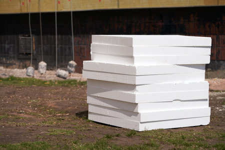 Insulating the facade of a multi-storey building. Stack of expanded polystyrene on the ground near the wall of the building. A layer of glass wool is already attached to the wall. Along the wall are the counterweights of the construction cradle.の写真素材