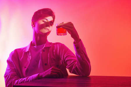 A man on an orange-purple background with a glass of whiskeyの写真素材