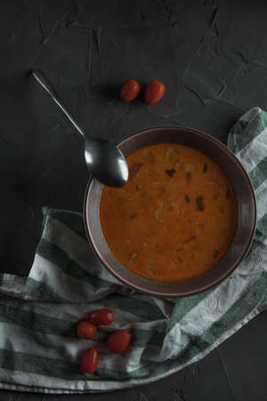 beautiful bowl of tom yam soup on a dark stone table. Nearby is a spoon, a beautiful towel and cherry tomatoes. Top viewの写真素材