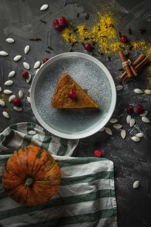 a delicious piece of pumpkin pie on a stone table, surrounded by cinnamon sticks, cranberries. In the background there is a pumpkin. Top view.の写真素材