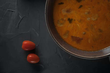 Cherry tomatoes next to a bowl of tom yum soupの写真素材