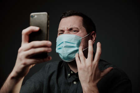 white young man, European, wearing a medical mask, angry, shouts into a cell phone. Ambulance does not go, problem with calling. Upset and anger.の写真素材