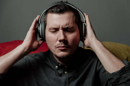 a young man, a European, on a sofa with pillows, enjoys music with headphones, showing a thumb up....