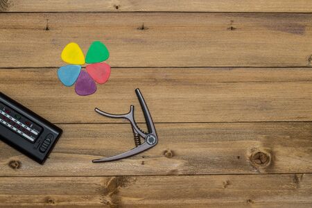 acoustic guitar and its accessories, capo, picks and tuner on wooden background