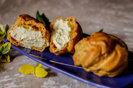 Delicious big cream puffs with cream in hand painted blue oval saucer with mint leaves on aged wooden background. Selective focus.の写真素材