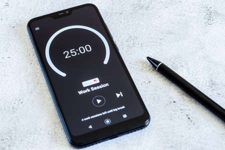 Demonstration of the Pomodoro Technique Time Management App. Hands to start the tomato timer on the smartphone screen. Used to improve workの写真素材