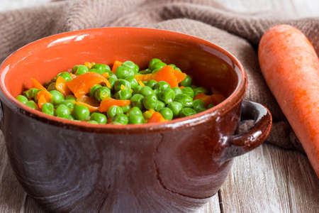 Green peas and carrots in small pan on wooden background.の写真素材