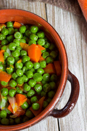 Green peas and carrots in small pan on wooden background.の写真素材