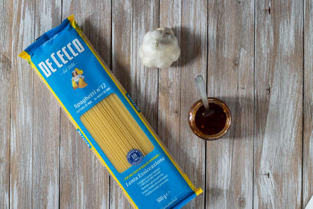 Italian De Cecco pasta in Spaghetti format with organic garlic and hot chilli pepper cut into pieces and placed in olive oil on dark wooden background.のeditorial素材