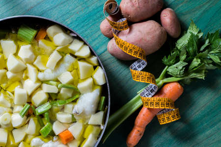 Boiled cod with potatoes, celery and carrots. Close-up of pan ready to cook, on green wooden...
