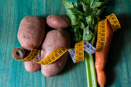 Potatoes, celery and carrots and a tailor's inch. Close-up on green wooden background. Christmas binge post diet concept.の写真素材