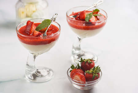 Two glasses of traditional creamy pudding dessert panna cotta with peppermint, strawberry jam, fresh strawberriesの写真素材