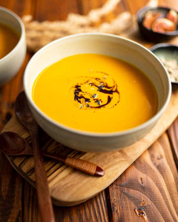 One gray bowl of pumpkin cream soup with pumpkin seed oil on wooden table and two wooden spoonsの写真素材