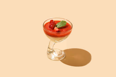 A glass of traditional italian creamy pudding dessert panna cotta with peppermint, strawberry jam, fresh strawberries with hard light shadowの写真素材