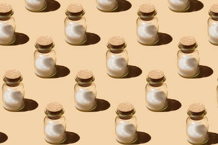 A hard light pattern of a glass jar with cork lids containing coarse sea salt on pastel yellow seamless surface in hard lightの写真素材