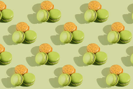 Hard light pattern of a macaroon pastry - two green ones and one orange - photographed on light green surfaceの写真素材