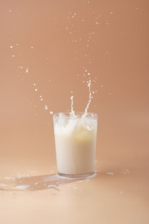 A glass of milk and splashes of milk on pastel yellow backgroundの写真素材