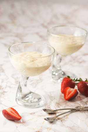 Two glasses with a traditional creamy pudding dessert panna cotta and surrounded by fresh strawberries on a marble surfaceの写真素材