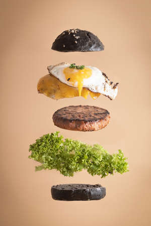 Levitating hamburger ingredients in black squid ink bun and vegan pea patty on pastel backgroundの写真素材