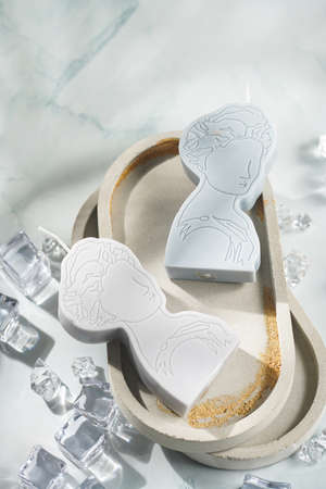 Two gray and blue candles shaped as greek goddess on a concrete tray and white crystals on pastel blue backgroundの写真素材