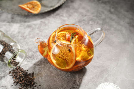 A transparent tea pot filled with black tea, oranges and mint on a gray surfaceの写真素材