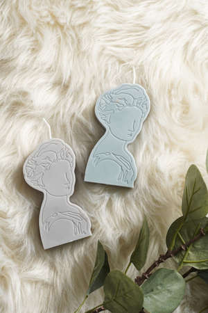 Two gray and blue candles shaped as greek goddess on a white faux fur surfaceの写真素材