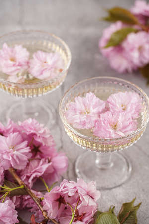 Two champagne glasses with splashes of champagne and pink cherry blossom on a gray surfaceの写真素材