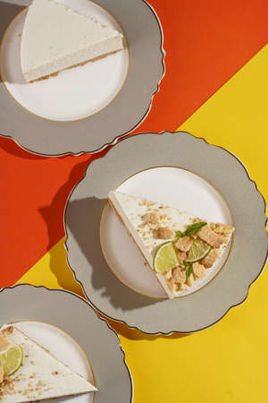 Three pieces of a lime cheesecake on romantic plates on a bright orange-yellow surfaceの写真素材