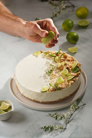 A male hand squeezing lime onto a big white lime cheesecake on a pastel blue surfaceの写真素材