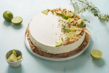 A big white lime cheesecake on a pastel blue surface surrounded by limes, butter cookies and flowersの写真素材
