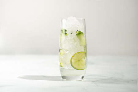 A tall long drink glass with cucumber, ice cubes and lime on a white backgroundの写真素材