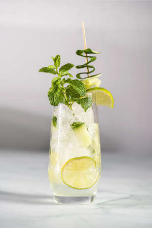A tall long drink glass with cucumber, mint, ice cubes and lime on a white backgroundの写真素材