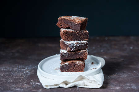Five pieces of brownie stacked on top of each other on a white plate on a dark backgroundの写真素材