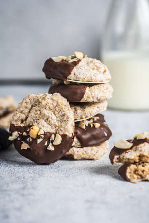 Almond half-chocolate biscuits sprinkled with chopped peanuts and placed on top of each other and milk bottle on light backgroundの写真素材