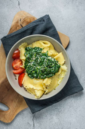 Ravioli with tomatoes and spinach in a gray bowl on a wooden board on a gray surfaceの写真素材