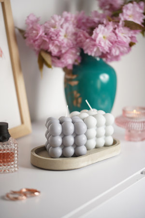 Two gray bubble candles on a concrete tray on a white surface with pink blossom in the backの写真素材