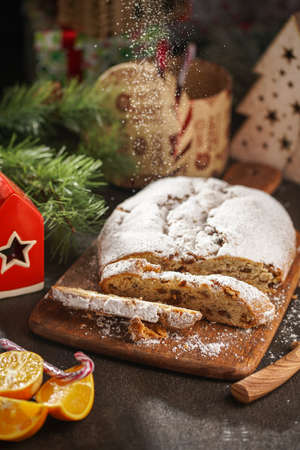 A traditional christmas pastry stollen with powdered sugar on a wooden board surrounded by festive decorationの写真素材