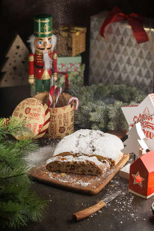 A traditional christmas pastry stollen with powdered sugar on a wooden board surrounded by festive decorationの写真素材