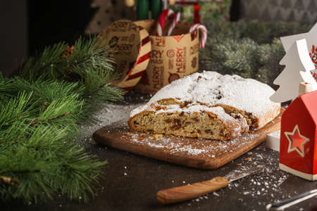A traditional christmas pastry stollen with powdered sugar on a wooden board surrounded by festive decorationの写真素材