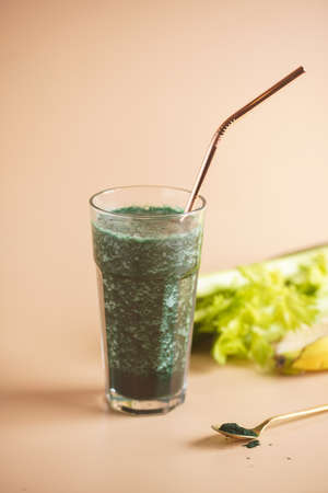 A glass of green healthy detox smoothie with vegetables and spirulina powder and a brass strawの写真素材